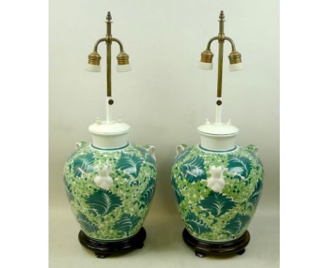 A pair of 20th century Chinese ceramic table lamps of triple handle vase form painted in shades of green with foliage, raised