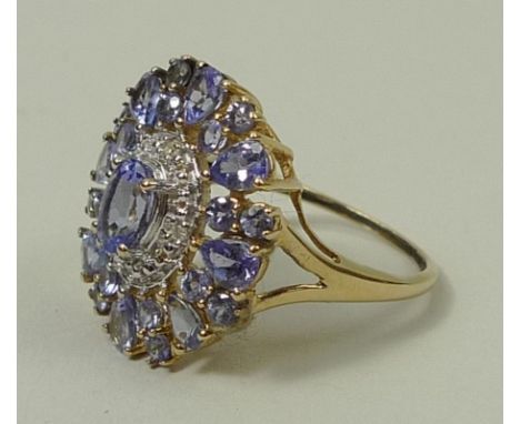 A tanzanite and diamond cluster ring, the pale lilac central tanzanite within a diamond set oval and flanked by a further eig