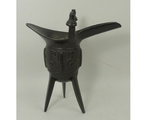 A Chinese cast patinated bronze wine vessel of archaic jue form, raised on three splayed feet, 17cm high. 