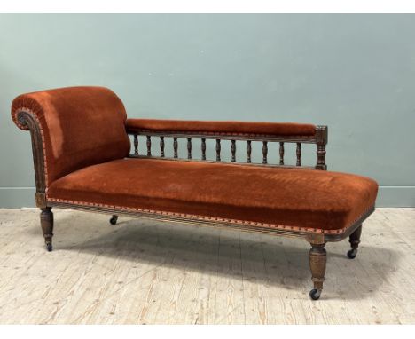 An Edwardian oak framed daybed/ chaise longue, upholstered in burnt orange velvet fabric, with turned spindle rail to back, r