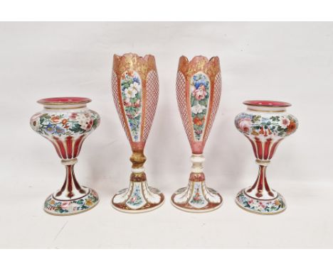 Two pairs of late 19th century Bohemian ruby tinted cased and enamelled vases, the first tapering oviform with petal shaped r