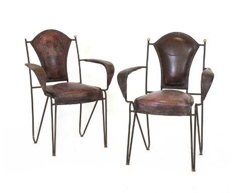 A pair of unusual iron and leather armchairs,probably French, each with polished brass finials, one missing, with a stitched 