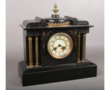 A decorative black slate mantle clock with column supports. Comprises of two holes and enamel dial with Arabic numerals. Come