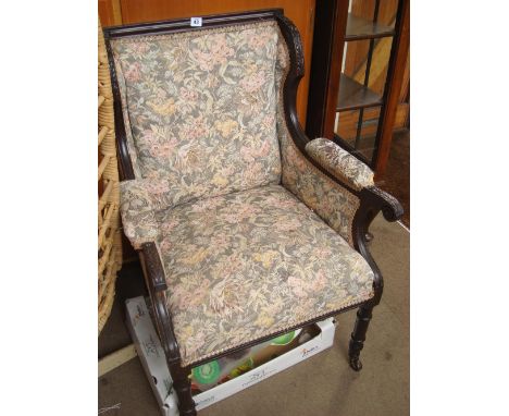 An Edwardian acanthus leaf carved mahogany framed wing armchair, with padded arms and scroll terminals, raised on fluted and 