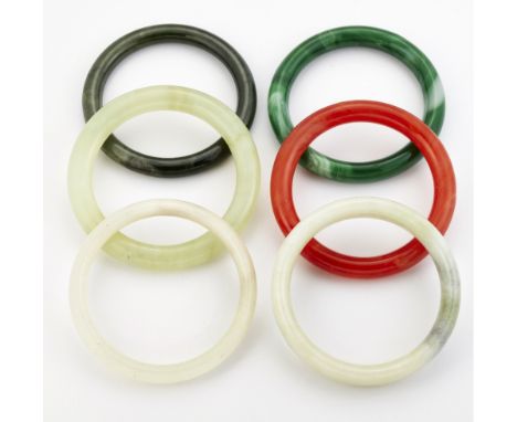 A GROUP OF FIVE JADE AND OTHER HARDSTONE BANGLES, AND A GREEN GLASS BANGLE. (6) 6.5cm diameter and smaller