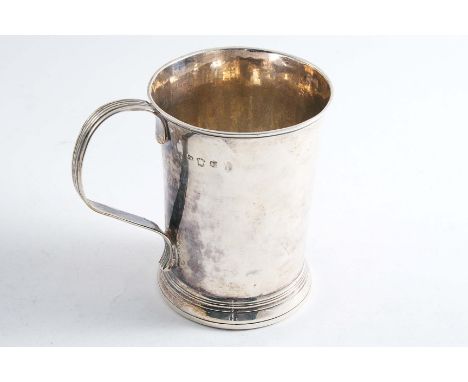 A GEORGE II MUG with a plain, flaring body, a reeded handle & a skirted base, inset with an iron ring and inscribed "T ASHWOR