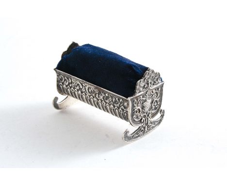 A LATE VICTORIAN NOVELTY PIN CUSHION in the form of a cradle with embossed decoration and the Royal Coat of Arms stamped in l