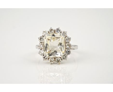 An 18ct white gold, unheated yellow sapphire and diamond cluster ring, the 7.31ct emerald cut pale yellow sapphire within a b