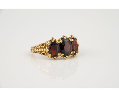 A 9ct gold and garnet three stone ring, Victorian style, with three graduated oval cut garnets, within foliate and bead borde