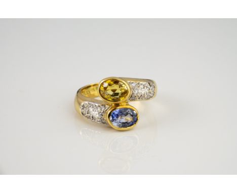 An 18ct gold, yellow &amp; blue sapphire and diamond cross over ring, the two oval cut sapphires over pavé set diamond should