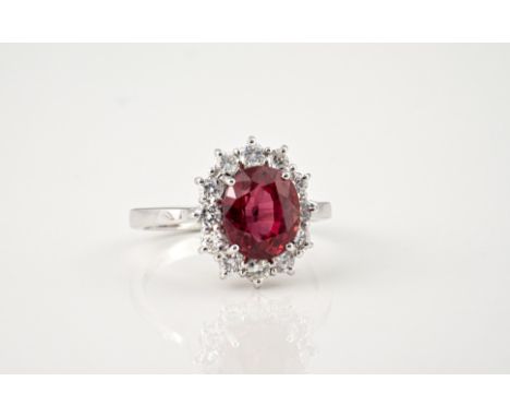 An 18ct white gold, ruby and diamond cluster ring, the oval cut 3.56ct ruby of fine colour, within a border of brilliant cut 