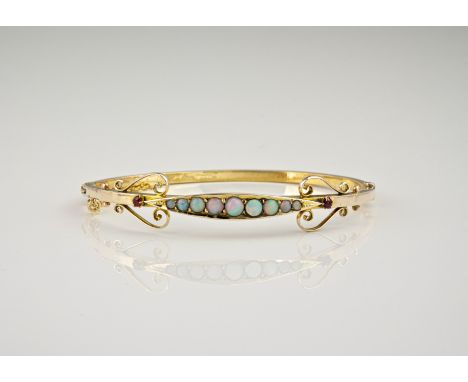 An Edwardian Art Nouveau style 9ct yellow gold, opal and ruby bangle, the central ellipse set with nine graduated opals, term