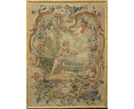 A French 18th century tapestry panel, depicting a boy in a garden landscape, within a mirror shaped border with sprays of flo