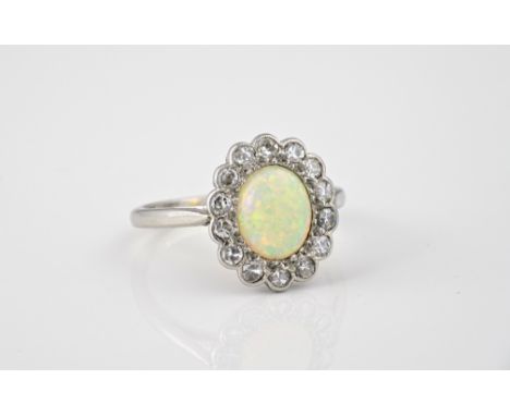 A mid-century platinum, diamond and opal cluster ring, the oval opal within a scalloped millegrain border with fourteen old b