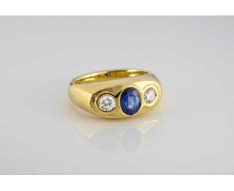 An 18ct gold, sapphire and diamond three stone ring, the central oval cut sapphire, 5.5 x 4.5mm., flanked by a pair of brilli