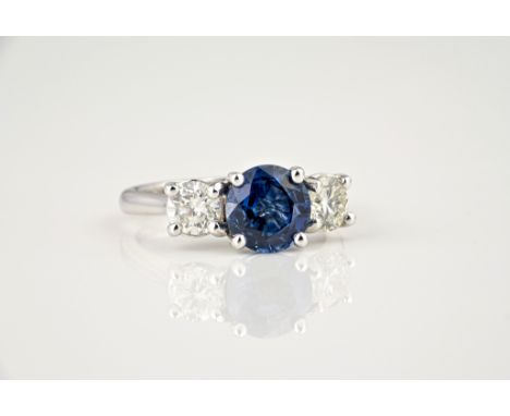 An 18ct white gold, sapphire and diamond three stone ring, the central 2.42ct round cut sapphire flanked by two brilliant cut