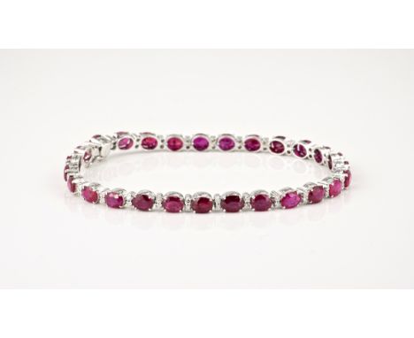 An 18ct white gold, ruby and diamond line bracelet, the twenty seven oval cut rubies, total 11.32ct, divided by pairs of bril