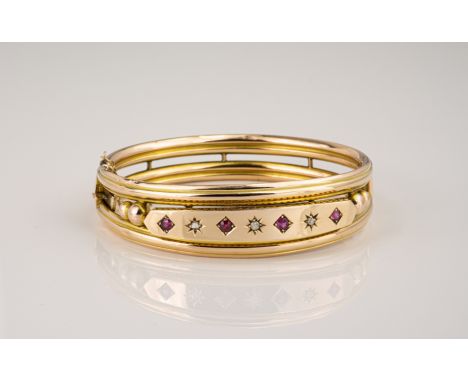 An Edwardian 9ct rose gold, ruby and diamond bangle, hallmarked Birmingham 1901, the hinged bangle set round cut rubies and r