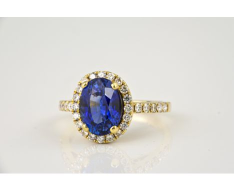 An 18ct yellow gold, sapphire and diamond cluster ring, the 4.13ct oval cut sapphire of fine colour, within a halo border of 