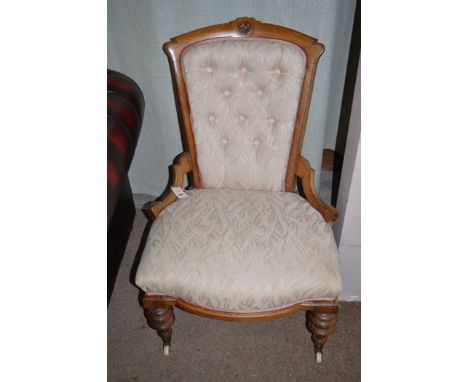 A Victorian walnut easy chair upholstered in pink and cream material, raised on turned legs terminating in ceramic castors.