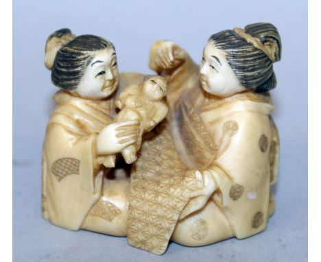 AN EARLY 20TH CENTURY SIGNED JAPANESE NETSUKE OF TWO KNEELING LADIES & AN INFANT, one of the ladies with a patterned swaddlin