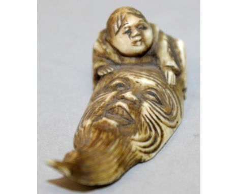 AN EARLY 20TH CENTURY JAPANESE IVORY NETSUKE, carved in the form of a boy kneeling before a large mask of Fukurokuju, 2.3in l