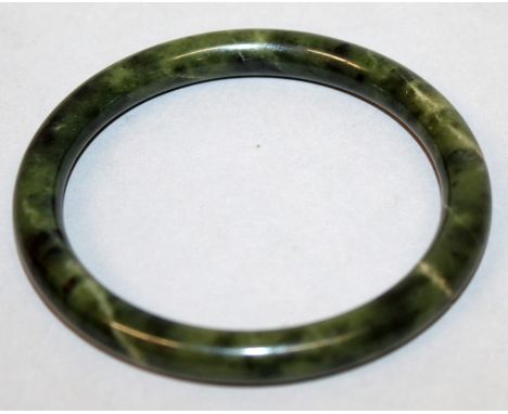 A CHINESE SPINACH GREEN JADE-LIKE BANGLE, the predominantly dark green stone with black and paler inclusions, 3.25in diameter