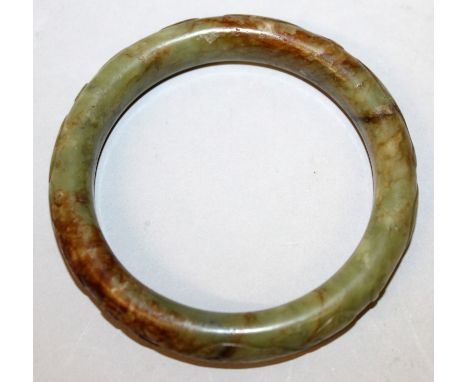 A CHINESE JADE BANGLE, the outer edge decorated in relief with sinuous chilong, the predominantly green stone with russet inc