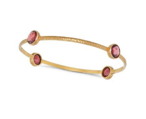 A PINK TOURMALINE BANGLE in 18ct yellow gold, the hammered gold bangle set with four fancy cut pink tourmalines, stamped 18K,