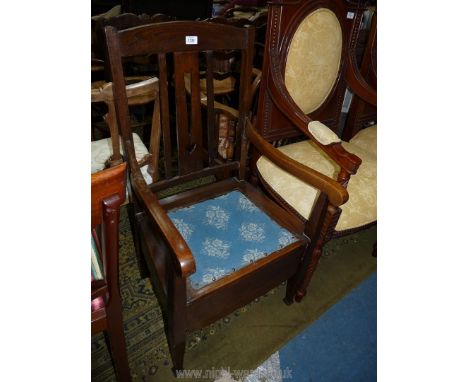 An Oak framed open armed Commode Chair with inset blue fabric upholstered seat, furnished.