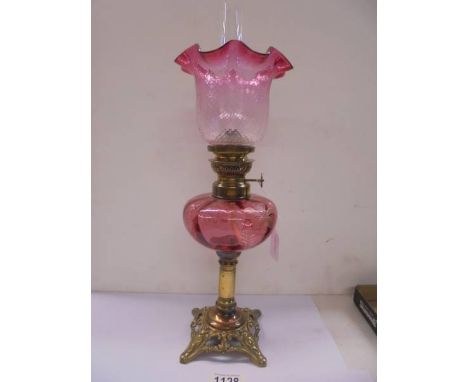 A Victorian oil lamp on a brass base with cranberry glass font and shade.