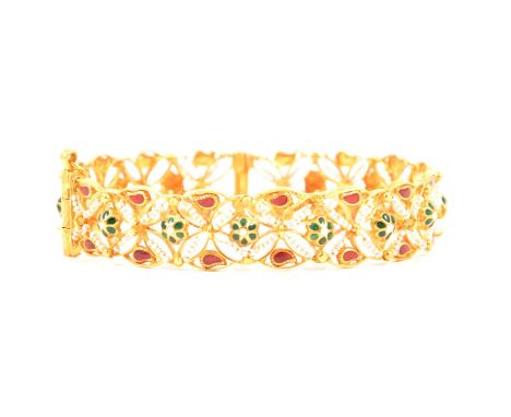 A yellow metal 12mm wide bangle with red and green enamel decoration simulating emeralds and rubies set with seed pearls, hin