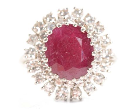 A ruby and diamond cluster ring, the oval mixed cut ruby approx. 11x4.9mm claw set and surrounded by two sets of eighteen rou