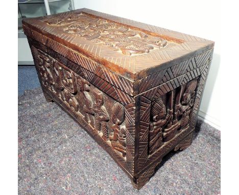 An African hardwood chest; the hinged top carved with a figure on horseback with musicians and an attendant etc., the front, 