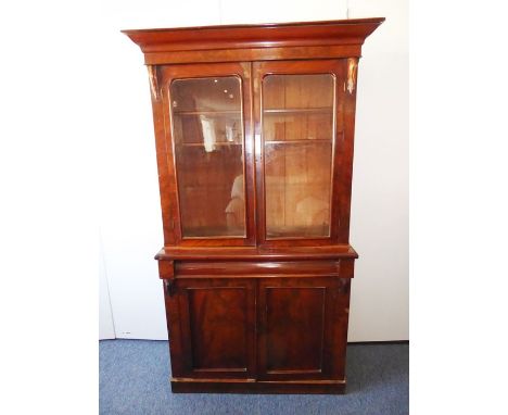 A 19th century mahogany bookcase, the outset cornice above two glazed doors enclosing shelves and flanked by carved volutes a