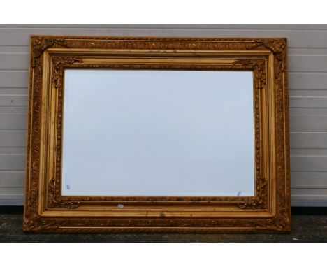 A large, ornately framed, bevel edge wall mirror, approximately 94 cm x 125 cm. [W]