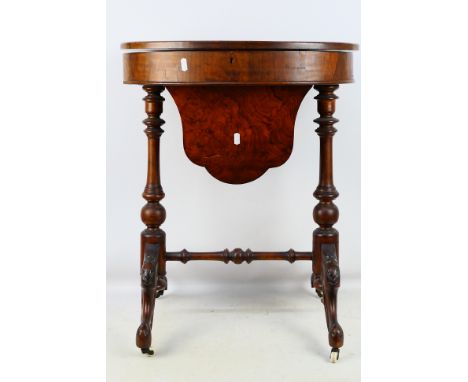 A burr wood veneered sewing table, the oval top on turned legs with carved decoration, raised on ceramic castors, 70 cm x 56 