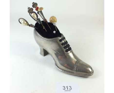 A pewter pin cushion in the form of a ladies shoe with various hat pins