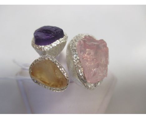 A rough cut three stone ring, the rose quartz, amethyst and citrine specimens in textured surrounds of unmarked white preciou