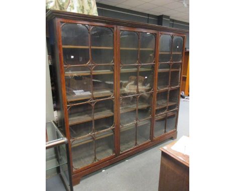 A mahogany bookcase with double cornice enclosed by three full length glazed doors with moulded glazing bars and bracket corn