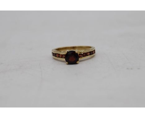 A vintage 9ct yellow gold and garnet flanked solitaire ring. Set to centre with a round mixed cut garnet in a four claw setti