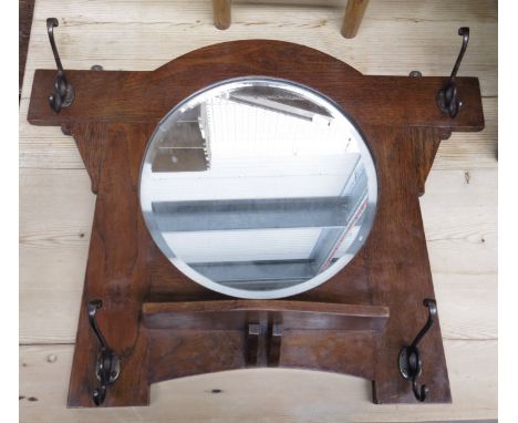 An Arts and Crafts oak hall mirror, incorporating hooks and a brush shelf, 50 by 68cm.