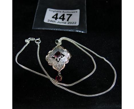 A sterling silver and garnet set lozenge form pendant, engine turned honeycomb decoration reserving a 9ct gold 'C' scroll bor