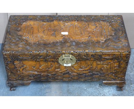 Chinese heavily carved camphor wood trunk with engraved brass lock raised on carved bracket feet, W70 x D35 x H34cm