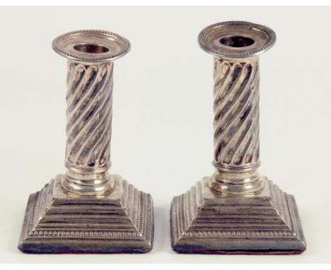 A PAIR OF VICTORIAN SILVER DWARF COLUMNAR CANDLESTICKS WITH SPIRALLY REEDED SHAFT ON STEPPED SQUARE FOOT, SHEFFIELD 1888, LOA