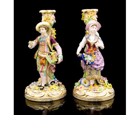 A pair of Minton candlestick figures of flower sellers, standing on a flower encrusted base before a column with a sconce att