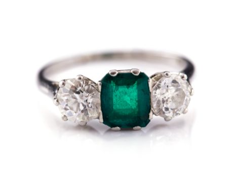 An emerald and diamond three stone platinum ring, the central emerald approximately 0.75 carat, the two round old cut diamond