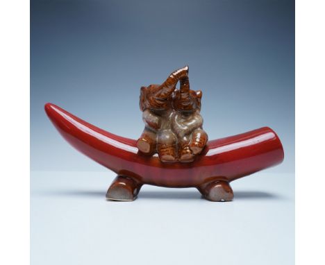 A charming glazed ceramic figurine featuring two playful elephants sitting atop a horn styled base. The elephants, depicted i