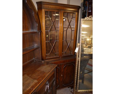 A reproduction mahogany corner display cabinet, with flared dentil cornice above two glazed panel doors enclosing shelves, fi