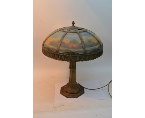 A large Art Deco gilt metal lamp, the coloured glass shade painted with a landscape, one replacement panel